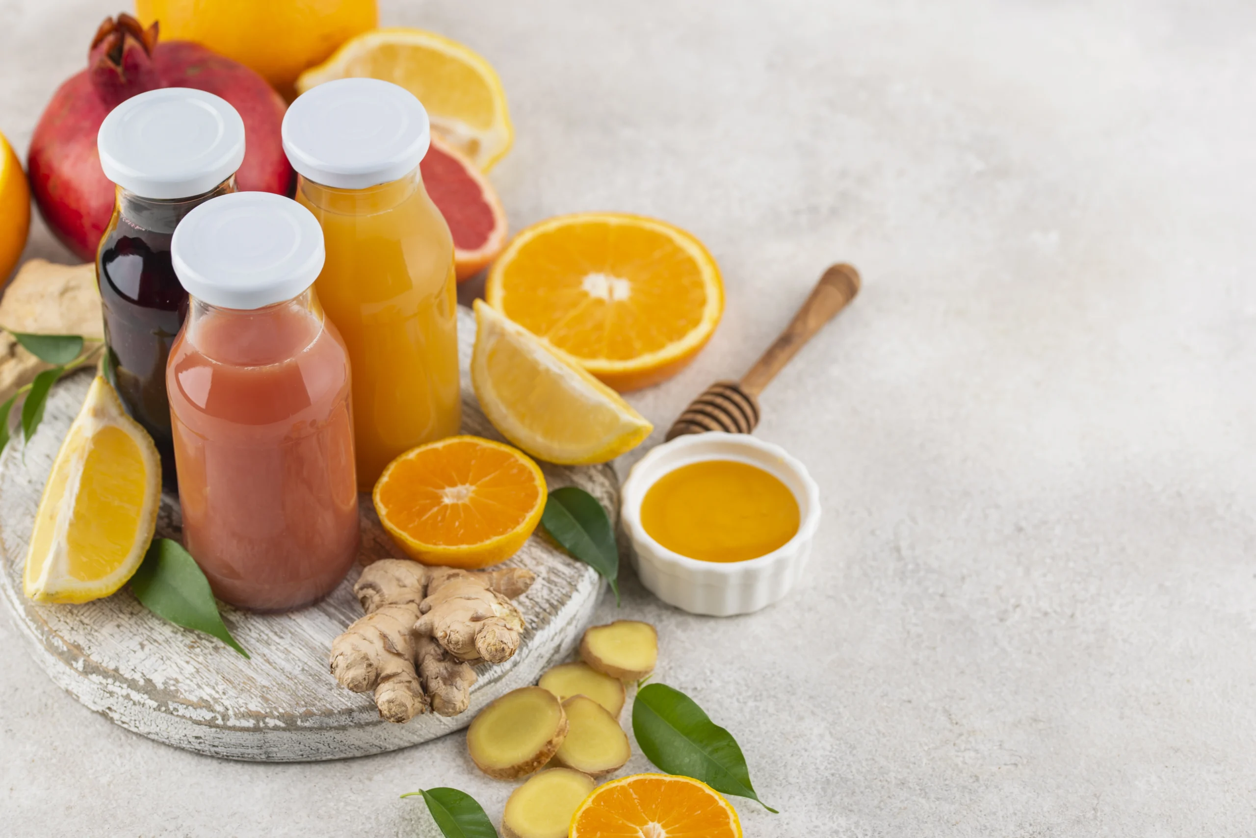 A variety of immunity-boosting juices in bottles, surrounded by citrus fruits, ginger, and honey. Caption: Freshly made immunity-boosting juices with citrus fruits, ginger, and honey for a healthy