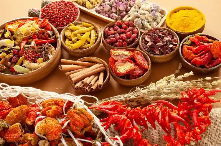 A colorful assortment of traditional Mauritian spices and dried ingredients including chillies, turmeric, cinnamon, herbs, and dried fruits displayed in wooden bowls.