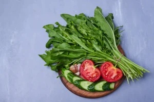 Fresh Mauritian brèdes UK style, tied on a wooden board with sliced tomatoes, cucumbers, and garlic, showcasing authentic Mauritian vegetables.